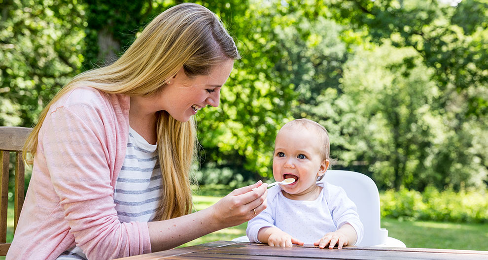 A woman feeds a baby outdoors.