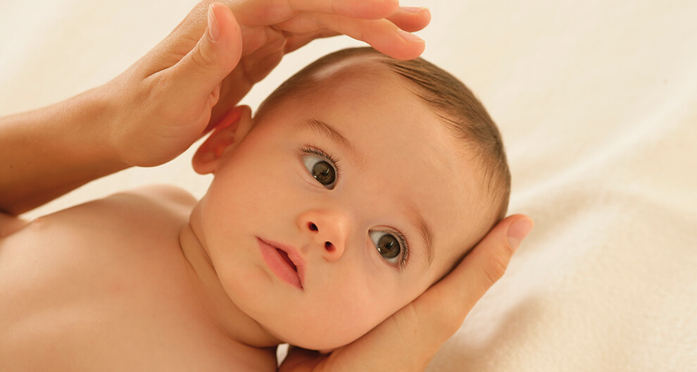 A hand gently cradles a baby's head.